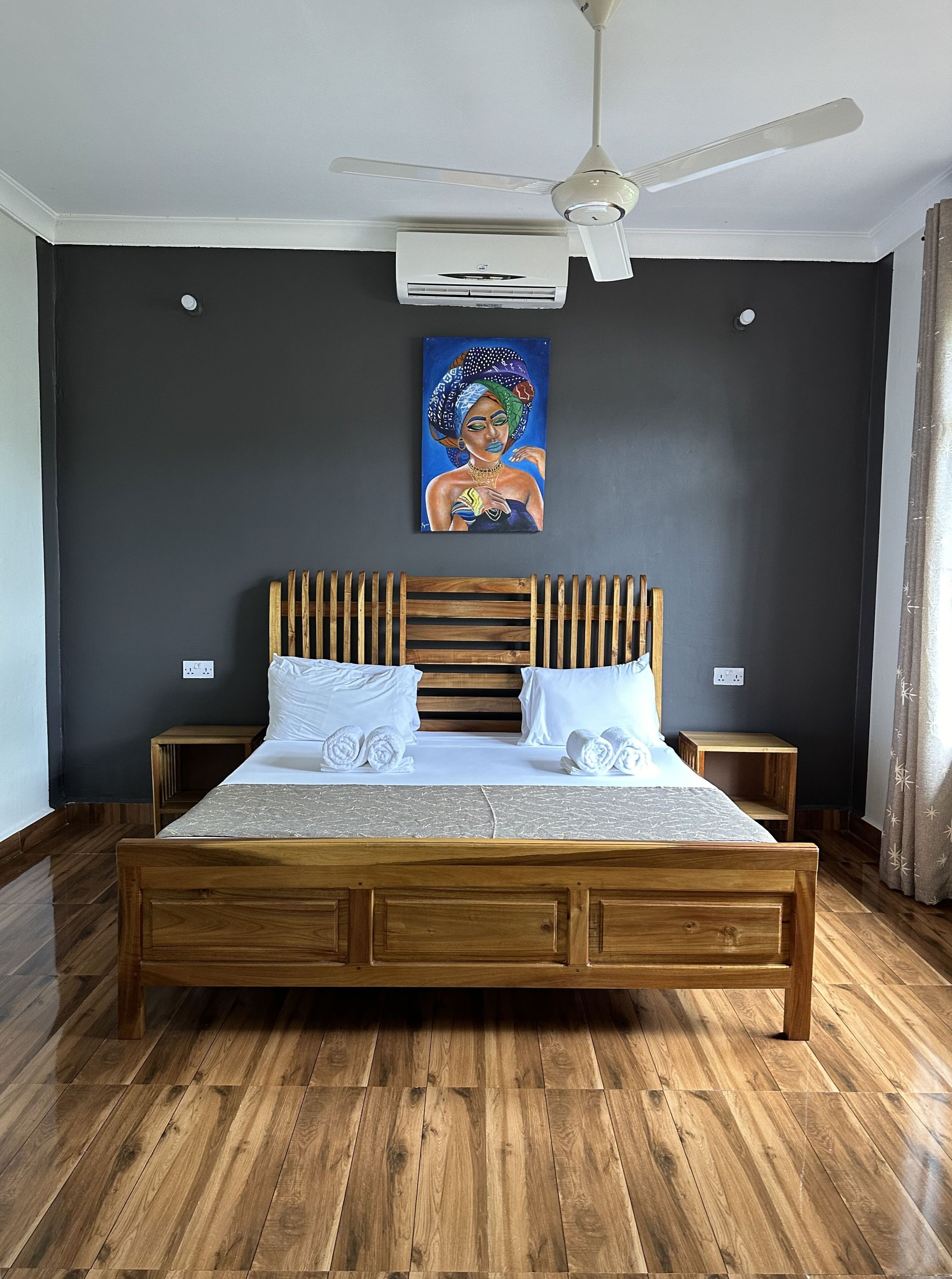 A bedroom with a wooden bed, white pillows, a ceiling fan, and an air conditioning unit.