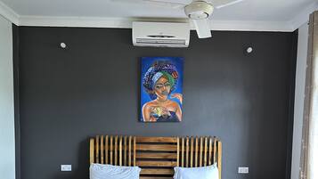 A bedroom with a wooden bed, white pillows, a ceiling fan, and an air conditioning unit.