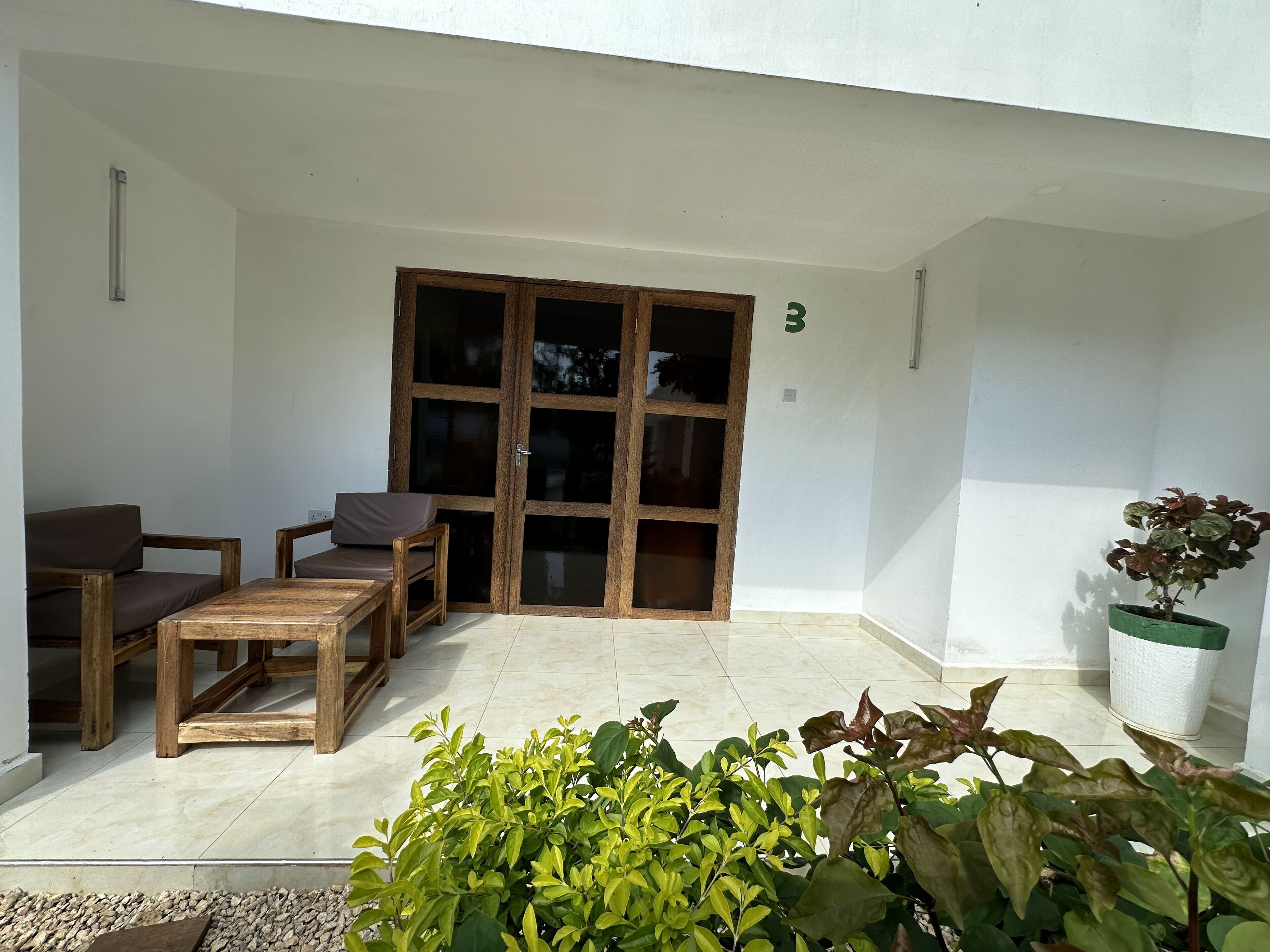 A covered patio area with a wooden table and two chairs, a potted plant, and a sliding glass door.