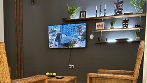Ein Wohnzimmer mit zwei Korbstühlen, einem kleinen Tisch und einem an der Wand befestigten Fernseher.