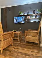 Una sala de estar con dos sillones de mimbre, una mesita y un televisor montado en la pared.