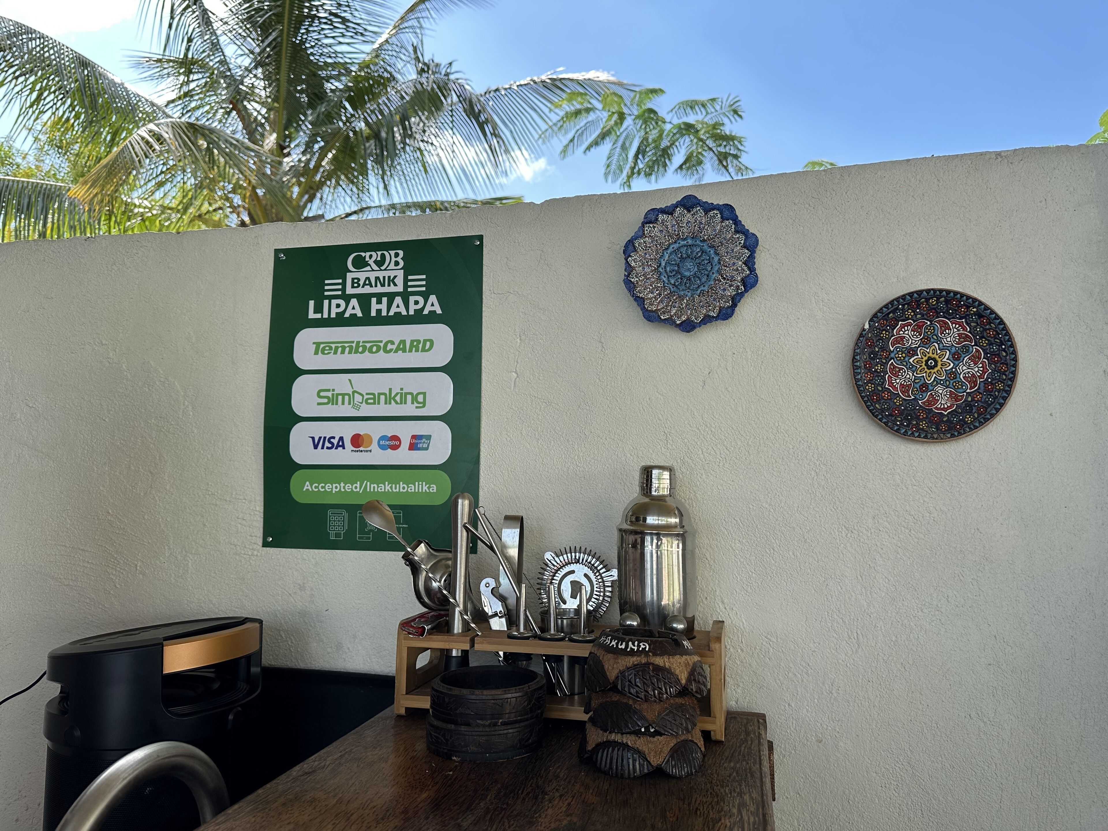 A wall with a sign listing accepted payment methods, a decorative plate, and a small table with a water bottle and utensils.