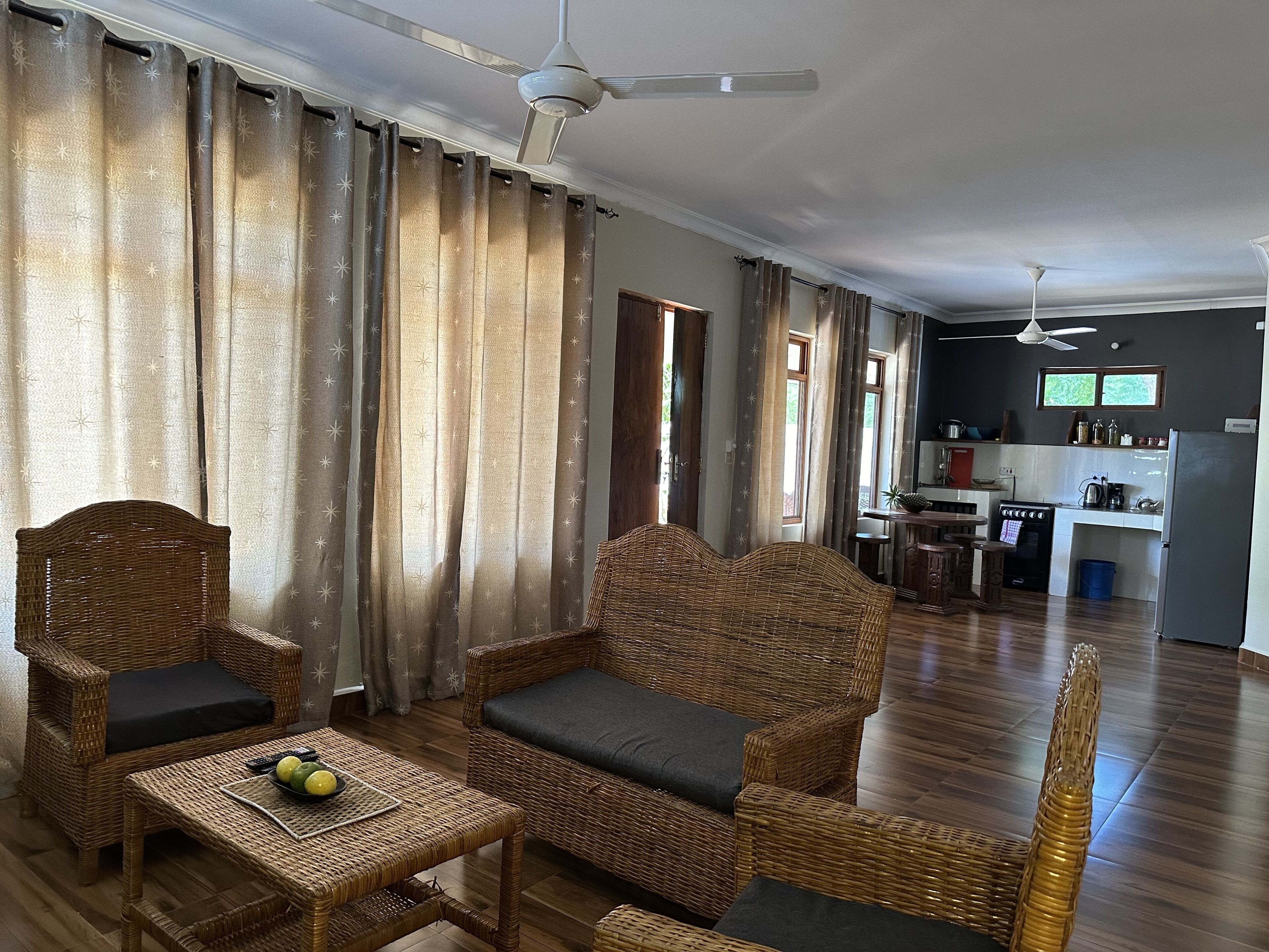 Amplia sala de estar con muebles de mimbre, una cocina al fondo y un ventilador de techo.
