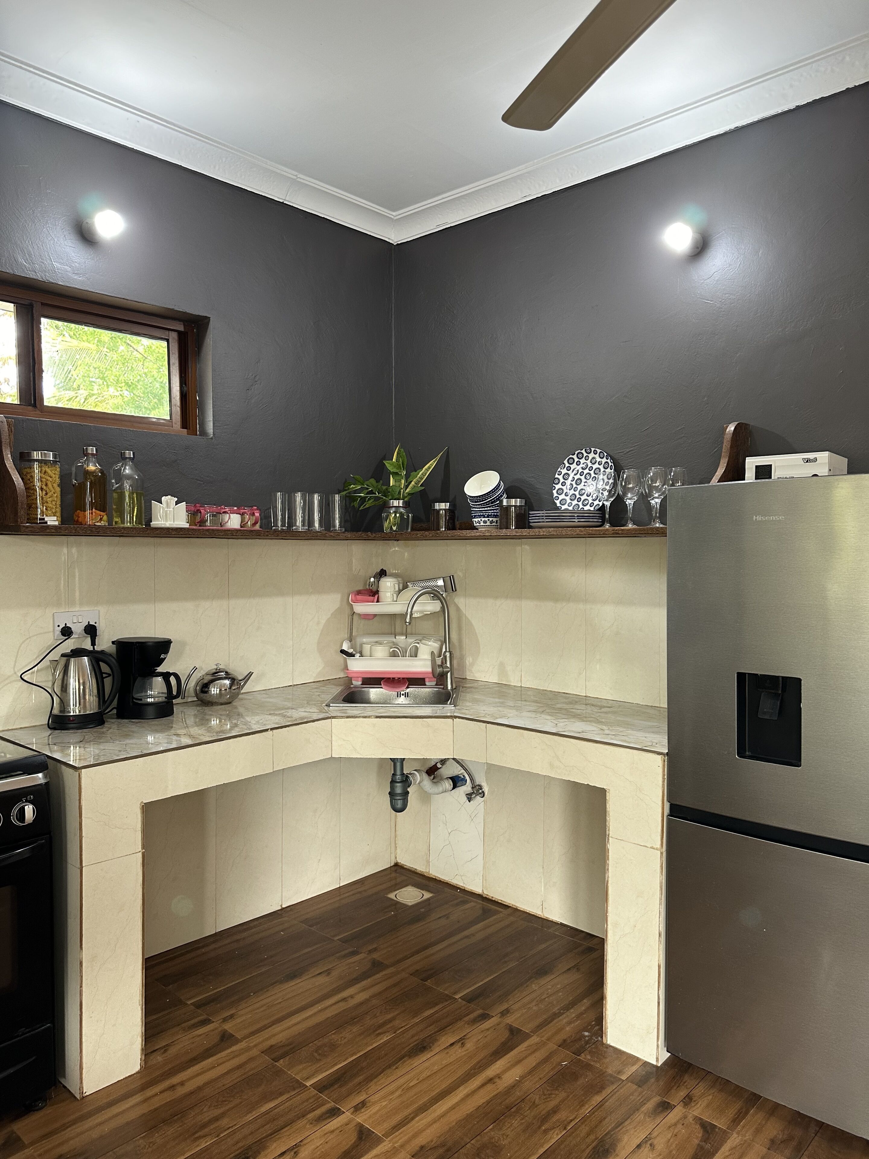 A kitchen with a corner sink, a stainless steel refrigerator, and a window above the sink.