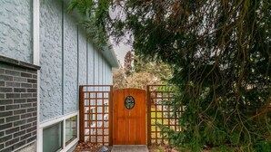 A wooden gate leading to a house with a brick foundation and a window.