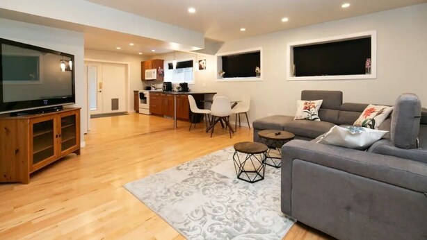 A modern living room with a grey sofa, a TV on a wooden cabinet, and a kitchen in the background.