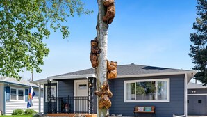 Un arbre auquel sont attachés plusieurs ours en peluche, une maison avec un porche et un drapeau en arrière-plan.