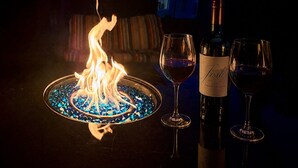 Un foyer avec des galets de verre bleus, une bouteille de vin et deux verres à vin posés sur une table.