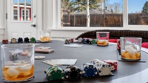 Une table de poker avec des jetons, des cartes et des verres contenant une boisson, le tout installé dans une pièce dotée d’une fenêtre donnant sur un jardin.