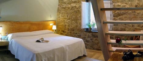 A bedroom with a bed, wooden headboard, stone wall, window, and a wooden table with a camera.