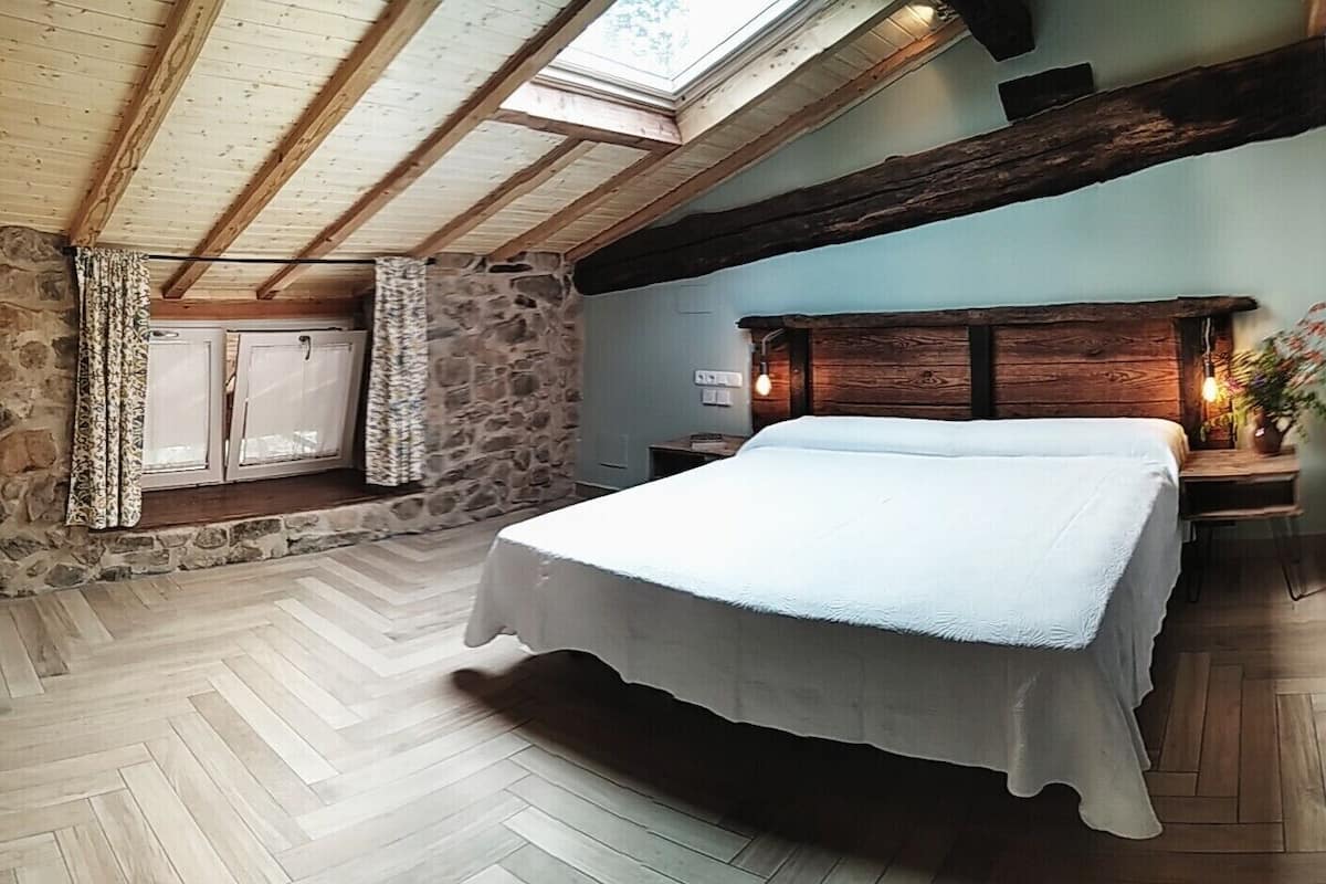 A bedroom with a bed, stone walls, wooden beams, and a skylight.