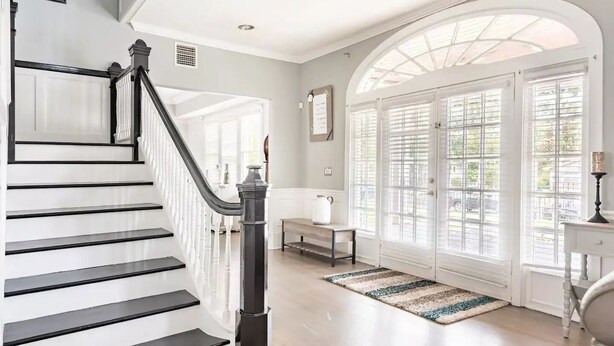 A staircase with black railings and a white wall. There is a bench and a table near a large window with blinds. - LUXURY 6000 sqft Mansion Downtown Orlando 6BR/5BA SLEEPS 14  Arcade Rooftop Deck (Orlando)
