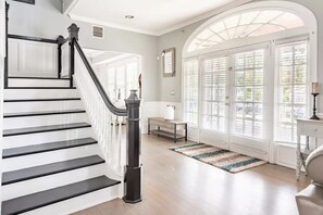 A staircase with black railings and a white wall. There is a bench and a table near a large window with blinds. - LUXURY 6000 sqft Mansion Downtown Orlando 6BR/5BA SLEEPS 14  Arcade Rooftop Deck (Orlando)