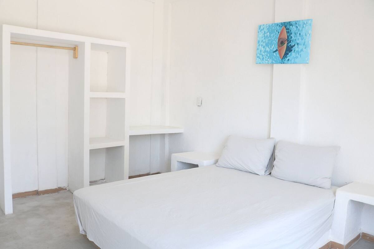 A bedroom with a bed, a white wardrobe, a nightstand, and a wall-mounted painting.