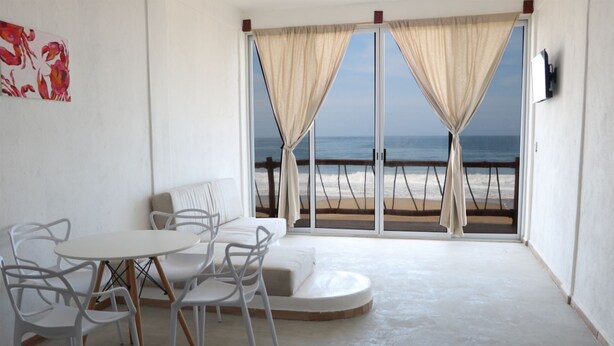 Una habitación con una mesa redonda y sillas, un sofá, y vistas a la playa a través de amplias puertas correderas.