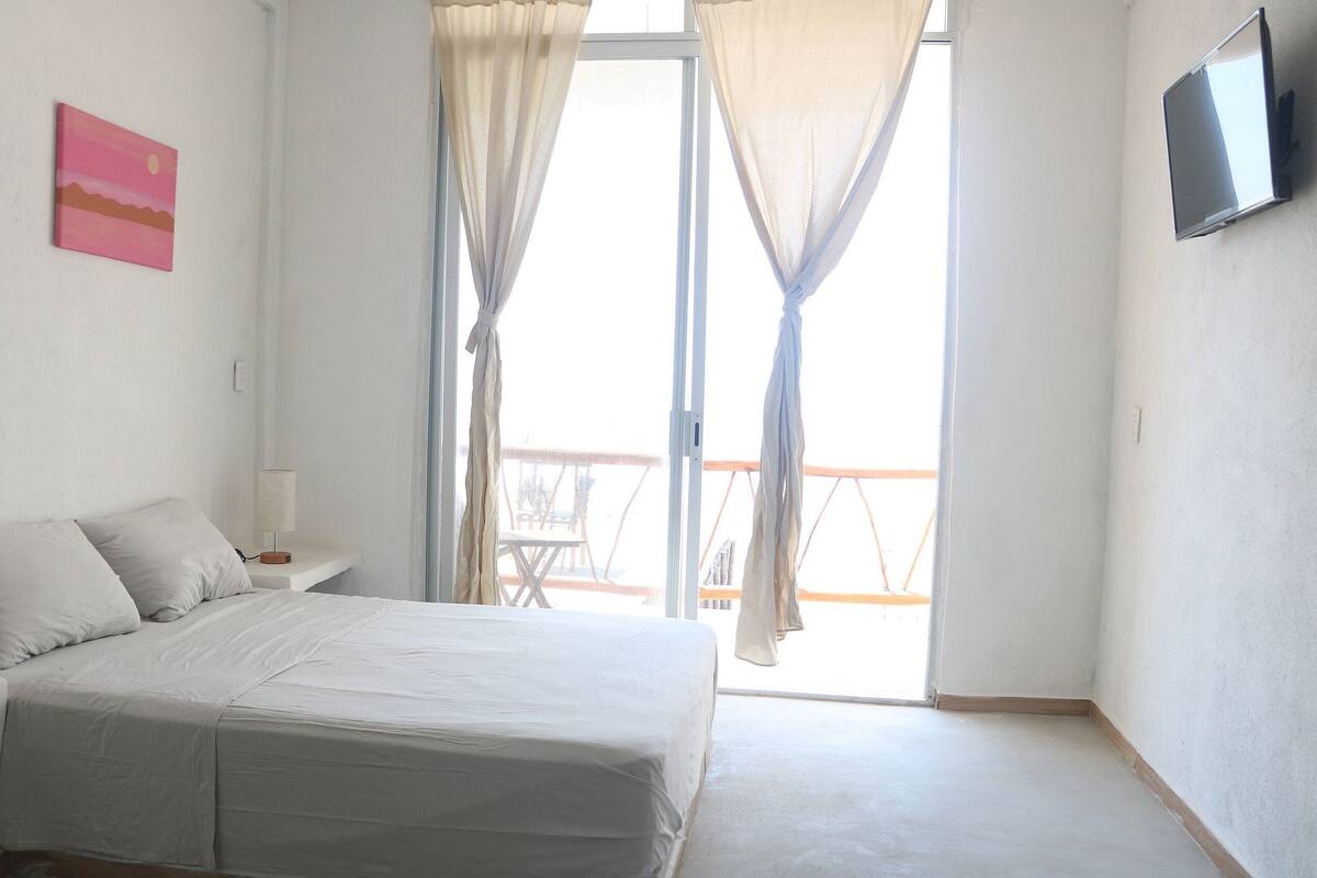 A bedroom with a bed, a nightstand, a TV, and a balcony with a table and chairs.