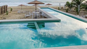Una piscina con borde de baldosas, rodeada de sillas y mesas de descanso.