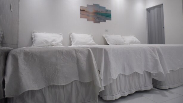A hotel room with two beds, white bedding, a painting on the wall, and a door with a window. - Casa Inteligente (Japaratinga)