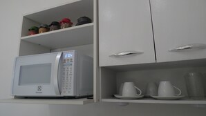 A kitchen with a microwave, shelves with jars, and cups. - Casa Inteligente (Japaratinga)