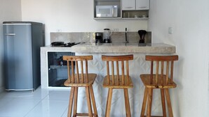 A compact kitchen with a refrigerator, stove, microwave, and bar stools. - Casa Inteligente (Japaratinga)