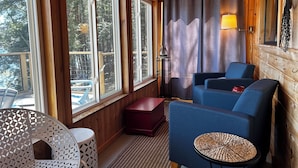 A cozy cabin interior with large windows, a seating area with blue sofas, a small round table, and a wooden ceiling. - Lakefront Cottage with Private Dock  and Kayaks. Dog-Friendly (Newfield)