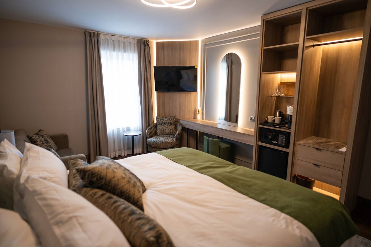 A hotel room with a large bed, a desk with a chair, a television, a wardrobe, and a mirror.