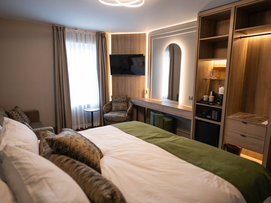 A hotel room with a large bed, a desk with a chair, a television, a wardrobe, and a mirror.
