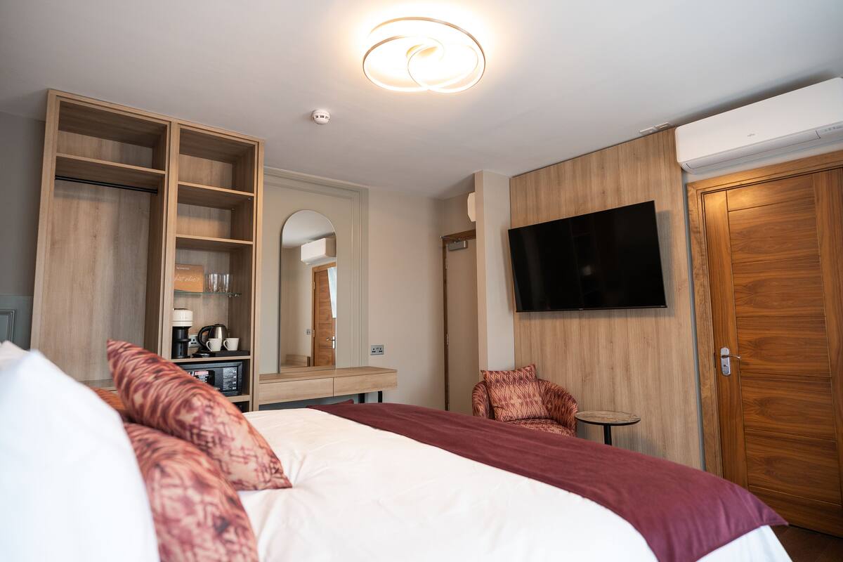 A hotel room with a large bed, a wooden wardrobe, a television mounted on the wall, and a small table.