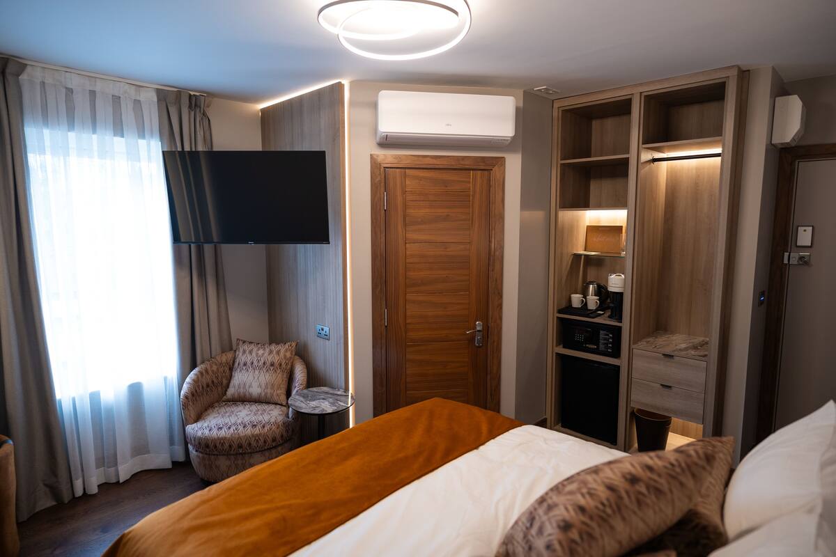A hotel room with a bed, a chair, a TV, a wardrobe, and a desk with a coffee machine.