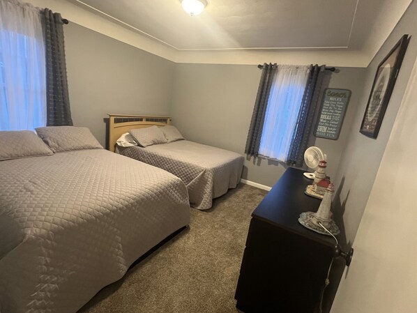 Une chambre avec deux lits, une commode et un ventilateur fixé au mur.