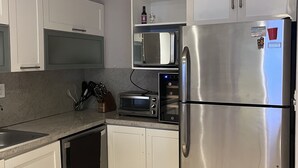 Une cuisine avec des armoires blanches, un réfrigérateur en acier inoxydable, un four à micro-ondes, un grille-pain et un ventilateur de plafond.