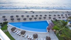 Un complexe hôtelier doté d’une grande piscine, d’une plage aménagée avec des parasols et de chaises longues.