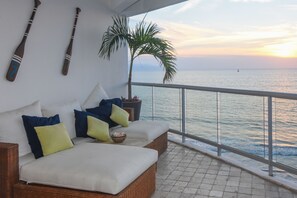 A balcony with a white cushioned sofa, a potted plant, and a view of the sea at sunset. - Beachfront Condo in Nuevo Vallarta (Nuevo Vallarta)