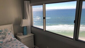Une chambre à coucher avec un lit, une table de chevet avec une lampe et une fenêtre donnant sur l’océan.