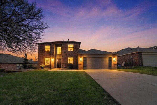 A two-story house with a garage, a driveway, and a well-maintained lawn. - The Haven - King Beds - Games - Office - BBQ - Yard (Forney)