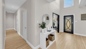 A hallway with a white console table, a mirror, and a door with a geometric design. - The Haven - King Beds - Games - Office - BBQ - Yard (Forney)