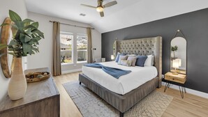 A bedroom with a large bed, a ceiling fan, a bedside table with a lamp, and a plant. - The Haven - King Beds - Games - Office - BBQ - Yard (Forney)