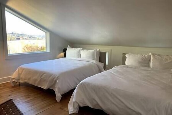 A bedroom with two beds, a wooden floor, and a window with a view.