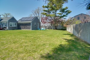 A backyard with a lawn, a wooden fence, and a house with solar panels. - Central Cape Cod Escape in South Yarmouth! (Yarmouth)