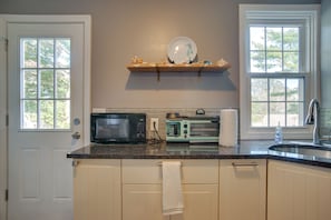 Compact kitchen area with microwave, toaster, and sink, featuring a countertop and cabinets.