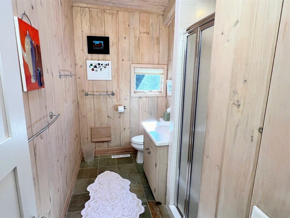 A compact bathroom with wooden walls, a white toilet, a sink, and a shower area.