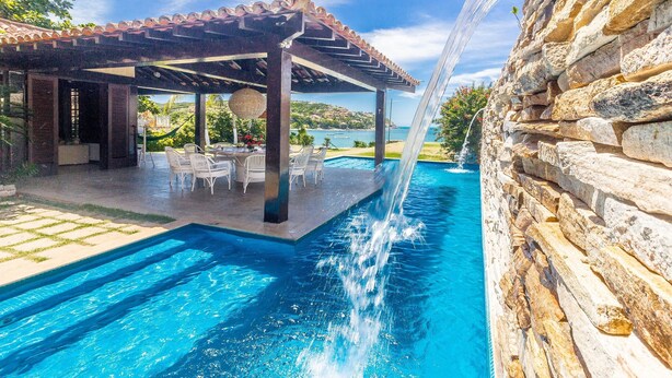 Una piscina con cascada, mobiliario exterior y un muro de piedra.