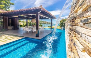 A swimming pool with a waterfall feature, outdoor seating, and a stone wall. - Casa com Cinco Quartos Pé na Areia (Búzios)