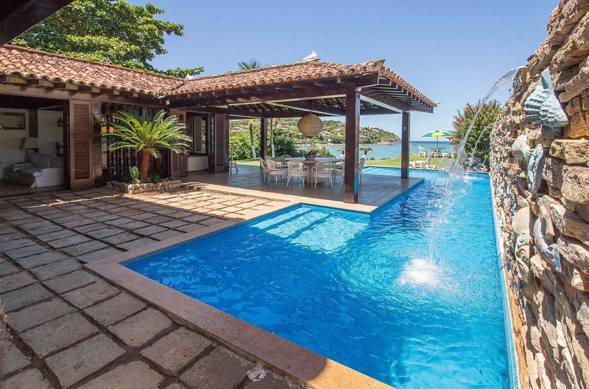 Una piscina con un muro de piedra y una pérgola con mobiliario exterior.