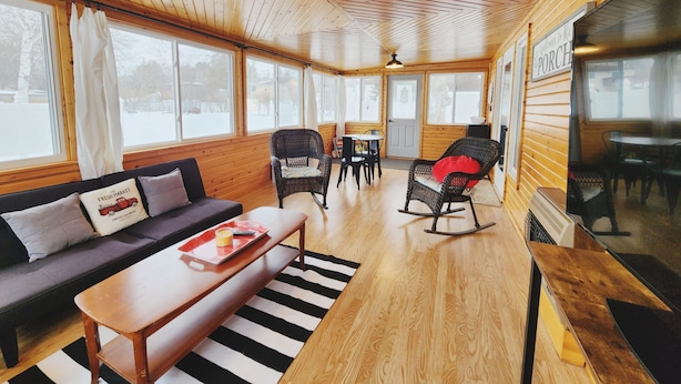 Ein gemütliches Blockhaus-Interieur mit Holzbalkendecke, einer Couch, einem Esstisch und einem Schaukelstuhl.