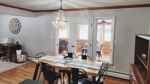 Ein Essbereich mit Holztisch, schwarzen Stühlen, einer Chandelierleuchte und Blick durch Glastüren auf eine Außenpatio.