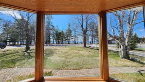 Ein Zimmer mit großen Fenstern und Blick auf eine grüne Fläche mit Bäumen und einer Straße.