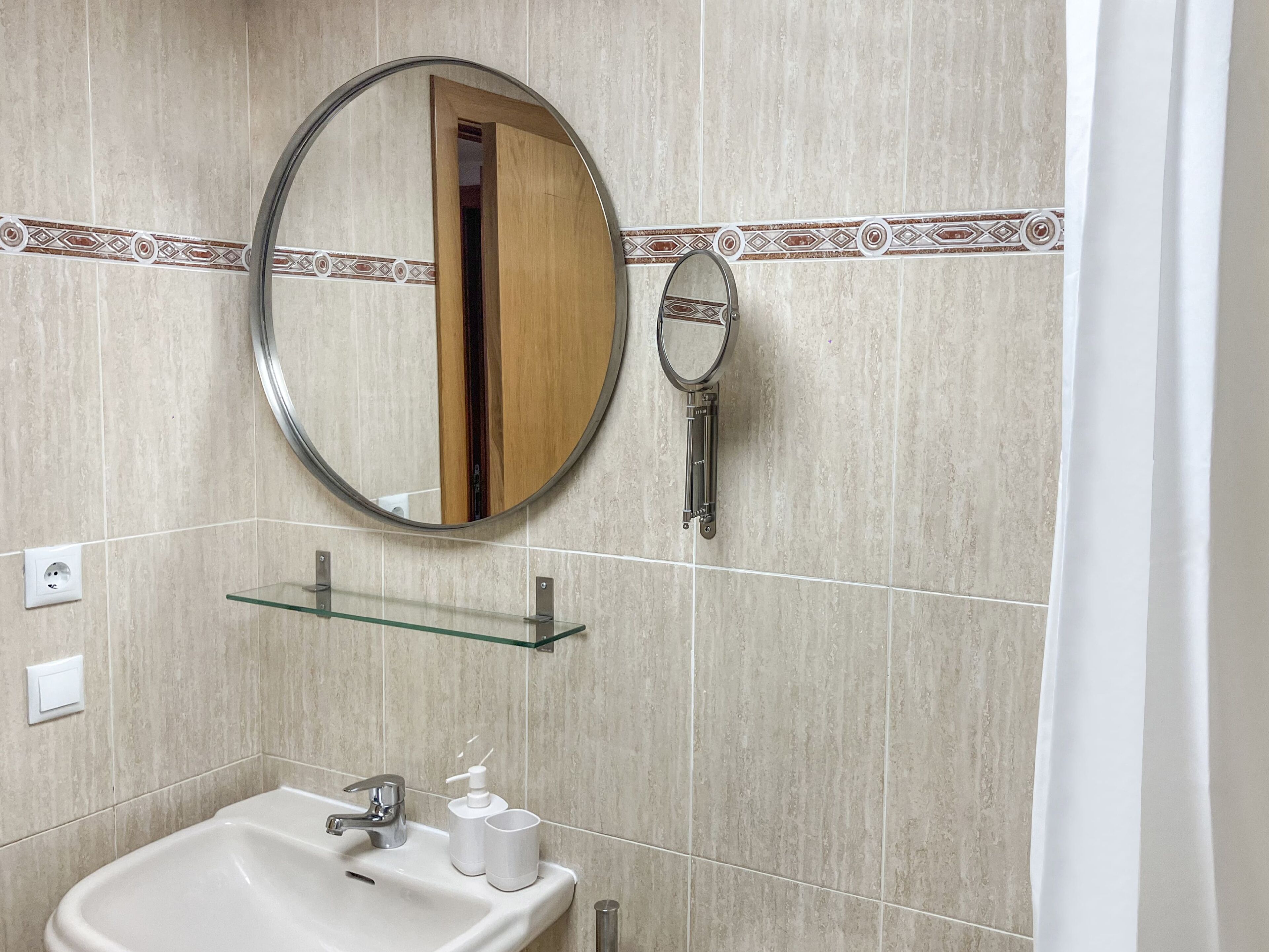 Un bagno con uno specchio rotondo, uno scaffale in vetro, un lavandino e un water.