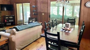Interior de una cabaña de madera con una mesa de comedor, sillas, un sofá, un televisor y una chimenea.