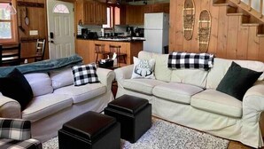 Interior acogedor de una cabaña con sala de estar que incluye dos sofás, una mesa de centro y una escalera que lleva a un nivel superior.